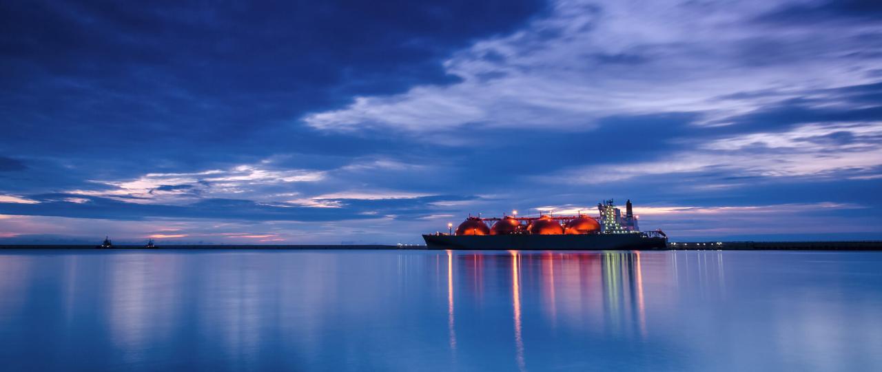 De lichten van de in de haven gelegen LNG-tanker Arctic Voyager, gezien vanaf zeeniveau, weerspiegelen in de schemering in het water.