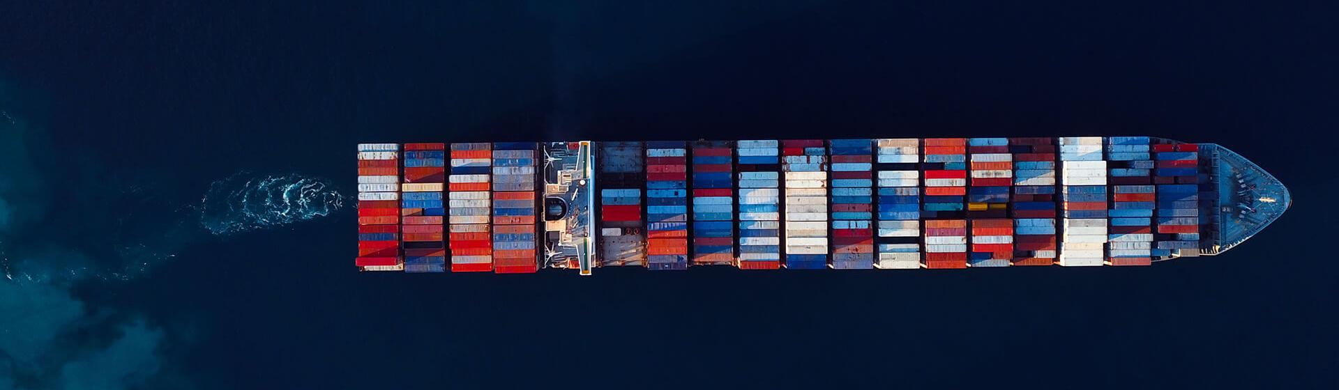 a cargo container ship from directly aloft moving into deeper water being approached by smaller vessel.