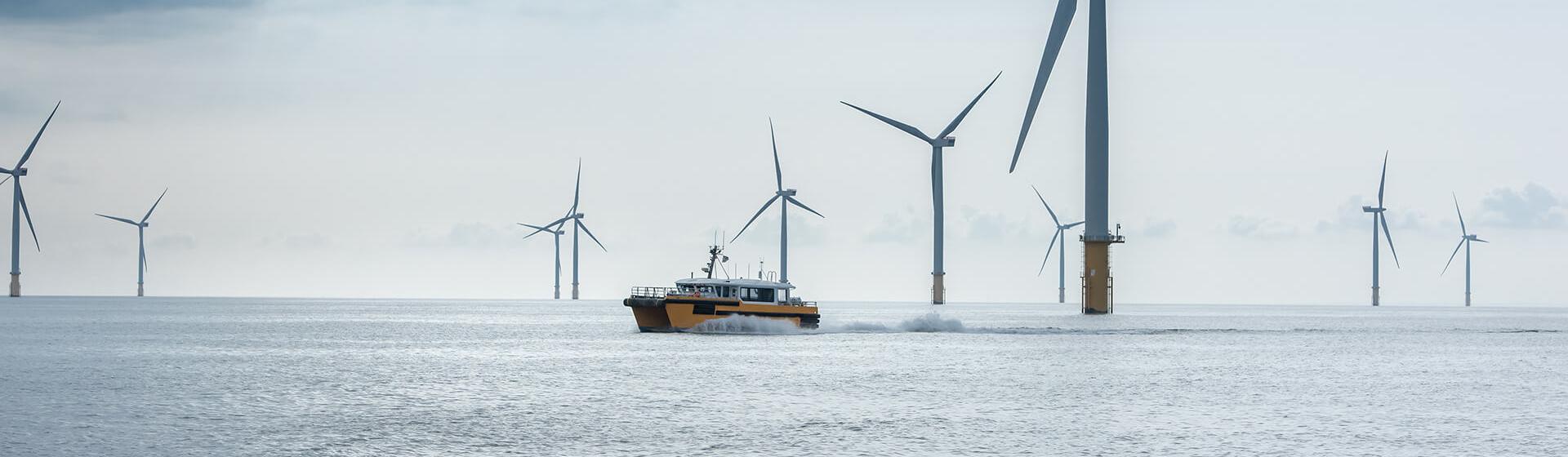 en offshore vindmøllepark. En servicebåt beveger seg fort mellom turbinene og etterlater seg et tydelig kjølvann.